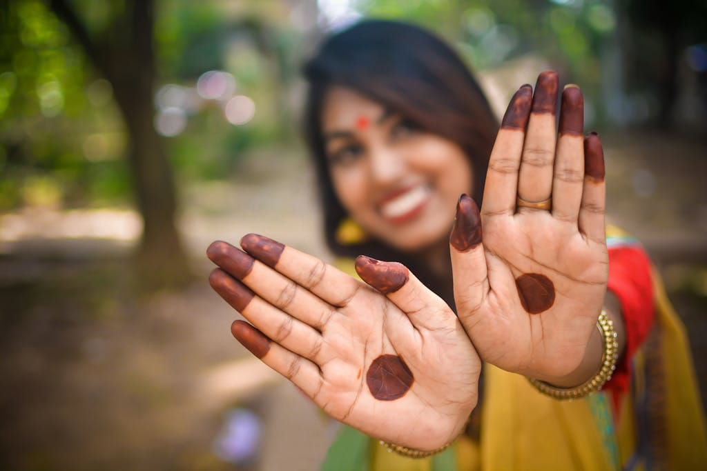 Close-up of a South Asian woman displaying henna on her palms with a vibrant smile and bokeh background.