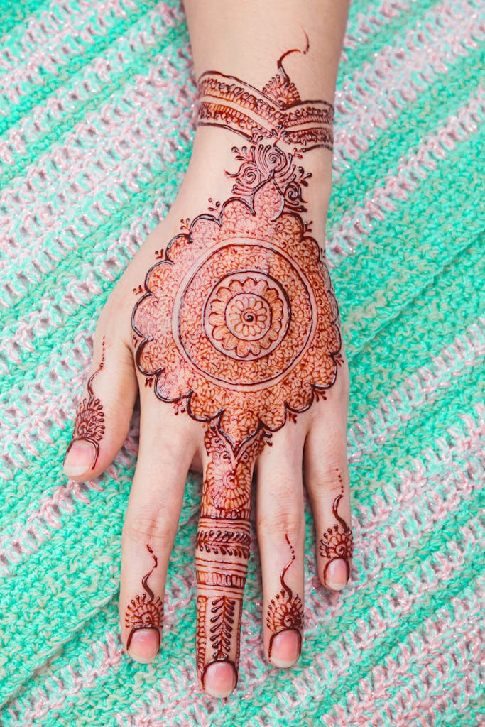 Detailed henna artwork on a hand with a colorful knitted textile backdrop, highlighting cultural artistry.