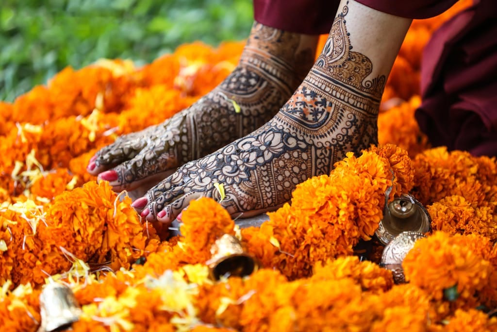 Beautiful mehndi-adorned feet surrounded by vibrant marigold flowers and ceremonial bells.